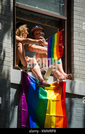 New York City - giugno 25, 2017: sostenitori arcobaleni onda bandiere da un appartamento che si affaccia su finestra annuale di Gay Pride Parade in Greenwich Village. Foto Stock