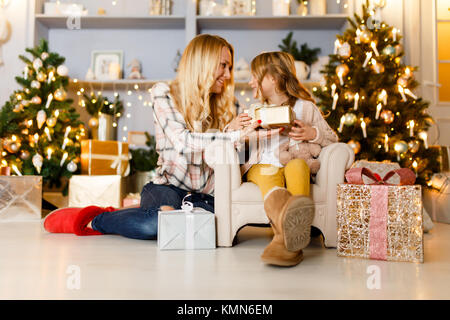 Nuovo Anno di immagine della madre dando dono alla figlia seduti su una sedia contro sullo sfondo di paesaggi, albero di Natale Foto Stock