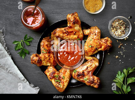 Alette di pollo fritte con salsa su sfondo scuro. Vista superiore, laici piatta Foto Stock