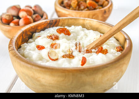 Latte di riso porridge con noci e uvetta in ciotole di legno su un bianco tavolo in legno Foto Stock