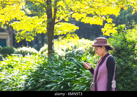 Tokyo, Giappone. 8 novembre 2016 - donna asiatica traveler ricerca di informazioni / mappa o in attesa di risposta a una chiamata sul suo smartphone nel giardino di primavera Foto Stock