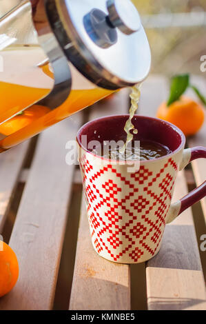 Versando il mandarino il tè in tazza sul tavolo di legno Foto Stock