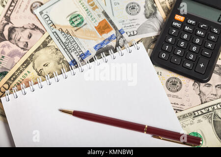 Blocco note con il foglio bianco, penna e calcolatrice su uno sfondo di diverse fatture del dollaro. Il concetto di pianificazione Foto Stock