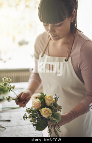 Giovani femmine fioraio mettendo insieme un bouquet di fiori misti mentre si lavora a un tavolo nel suo negozio di fiori Foto Stock