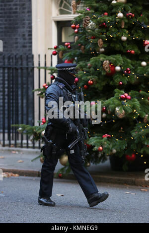 Un agente di polizia armato cammina davanti a un albero di Natale al di fuori della porta di 10 Downing Street a Londra. Foto Stock