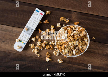 Caramello popcorn con il telecomando della tv su un tavolo di legno sfondo. il popcorn in una ciotola e telecomando TV. guardando film snack-NOZIONE Foto Stock