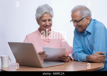 Felice coppia senior utilizzando laptop e guardando i documenti seduta sul tavolo Foto Stock