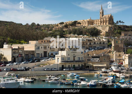 Il porto e dal terminal dei traghetti di Mgarr a Gozo che mostra gli edifici eun chiesa sulla città e le barche nel porto Foto Stock