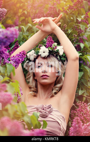 La perfetta donna bionda con fiori lilla e luce solare all'esterno. Bellissimo modello di moda su sfondo floreale Foto Stock