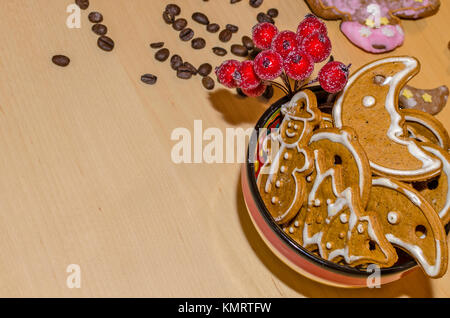 Gingerbreads Natale con glassa bianca in una ciotola colorati, i chicchi di caffè e rowan ramoscello per decorazione su una tavola di legno Foto Stock