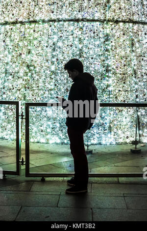 Una silhouette di un giovane uomo contro le luci di un albero di Natale in Madrid. Foto Stock