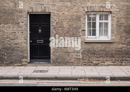 Parte anteriore nera porta in un edificio restaurato del muro di mattoni di una casa Vittoriana edificio residenziale con il bianco in legno finestra a ghigliottina Foto Stock