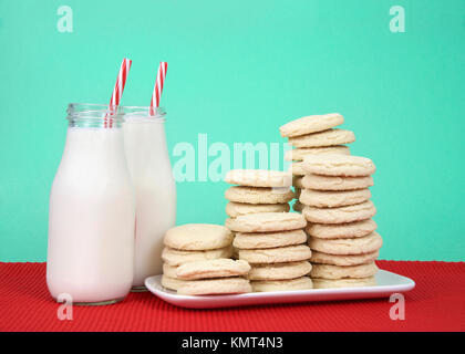 I cookie di zucchero sovrapposti ad altezze multiple su un bianco piastra rettangolare red placemat, sfondo verde. Due bottiglie di latte accanto alla piastra con rosso e Foto Stock