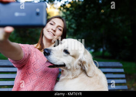 Foto della ragazza su banco facendo selfie con retriever Foto Stock