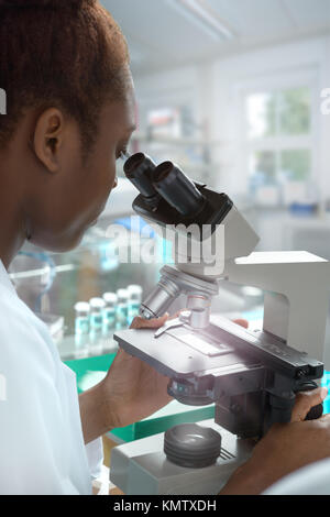 African-american donna scienziato o studente laureato in camice funziona con un microscopio in laboratorio moderno Foto Stock