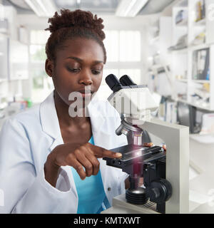 African-american donna scienziato, studente o tech in camice da laboratorio con opere in moderno laboratorio con un microscopio Foto Stock