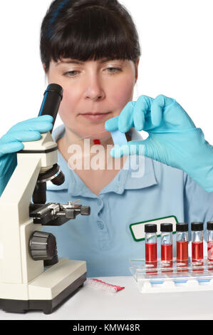 Ritratto di una giovane donna scienziato rosso analizzando i campioni di liquido sotto il microscopio. DOF poco profondo, focus sul vetro. Foto Stock