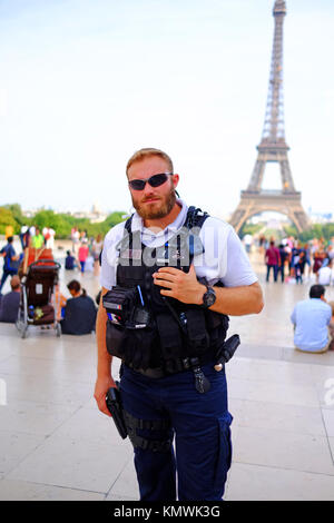Un poliziotto armato rimane messaggio di avviso durante la sua foto viene scattata e la sua mano è sulla sua pistola, mentre di pattuglia fra i turisti alla Torre Eiffel a Parigi Foto Stock