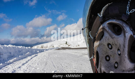 Primo piano delle catene da neve montate su una vettura nevoso la ruota con la copia di grandi dimensioni spazio sulla sinistra. Foto Stock