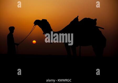 Uomo che guarda il suo cammello durante il tramonto khuri dune nel deserto di Thar vicino a jaisalmer in Rajasthan in India