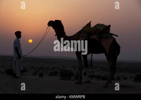Uomo che guarda il suo cammello durante il tramonto khuri dune nel deserto di Thar vicino a jaisalmer in Rajasthan in India