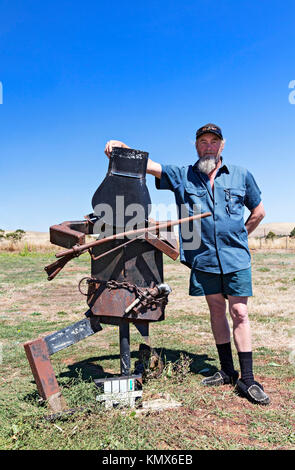 Un uomo australiano si erge orgogliosamente accanto alla sua bizzarra Creazione casella postale in Waubra Victoria Australia. Foto Stock