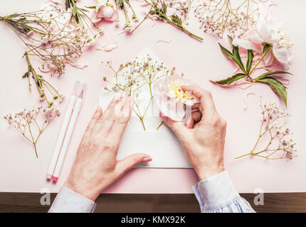 Mani femminili facendo bella composizione floreale con fiori in busta aperta su un colore rosa pallido sfondo, vista dall'alto. Creative saluto, invito e holi Foto Stock