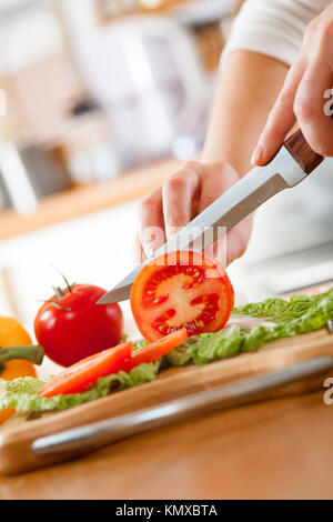 Donna con le mani in mano il taglio di pomodoro fresco su cucina Foto Stock