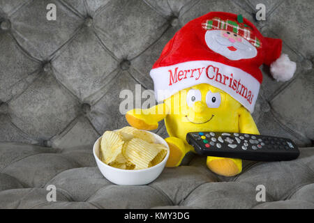 Concetto di immagine di una festa di Natale a guardare la televisione - giocattolo morbido con il telecomando della TV e ciotola di patatine. Foto Stock