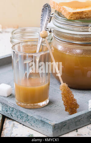 Vasetto di in casa la salsa di caramello, servito con cubetti di zucchero su un tavolo di legno Foto Stock