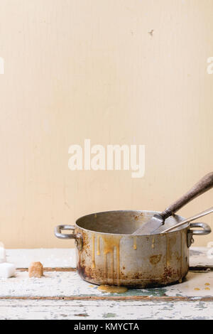 Vecchia vaschetta di alluminio di in casa la salsa di caramello, servita con cucchiai e cubetti di zucchero bianco su un tavolo di legno Foto Stock