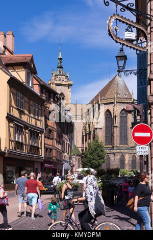 Turisti in Rue de l'Église con le tradizionali Maisons à Colombages (case in legno) e la chiesa di San Martino a Colmar, Alsazia, Francia Foto Stock