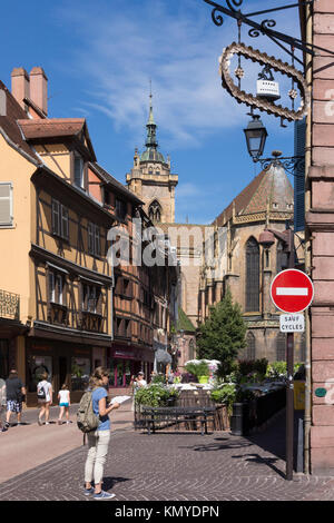 Un turista consulta una mappa di Rue de l'Église con le tradizionali Maisons à Colombages (case in legno) e la chiesa di San Martino a Colmar, Alsazia Foto Stock