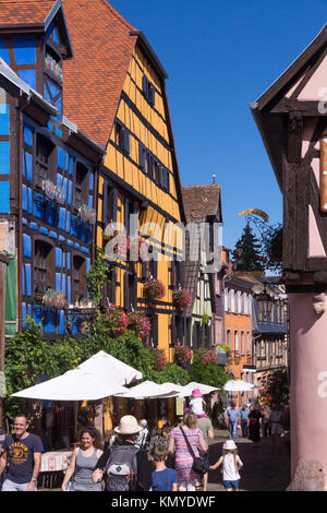 I turisti affollano tra maisons à colombages (metà case con travi di legno) in Riquewihr, una popolare destinazione turistica sulla Route des Vins in Alsace Foto Stock