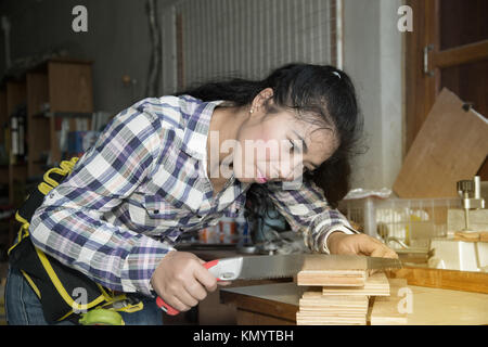 Bella donna asiatica utilizzando una sega a mano per tagliare alcuni di legno in un negozio di legno. Foto Stock