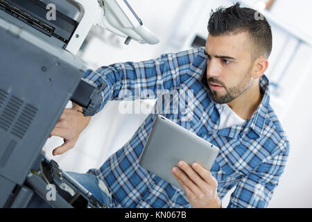 L'uomo sporgendoti fotocopiatore aperto durante le riparazioni di manutenzione Foto Stock