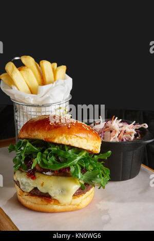 Succosa hamburger di manzo con salsa di lingonberry, formaggio fuso, rucola servito con patate fritte e cavolo rosso Foto Stock