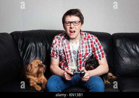 Un giovane uomo in una camicia rossa e jeans blu si trova a casa e gioca giochi video insieme con il loro cane. Urlando ragazzo nella parte anteriore della tv nel tentativo di combattere wit Foto Stock