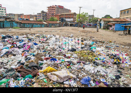 Un gran mucchio di plastica e i rifiuti generici spazzatura si trova nel bel mezzo di una zona aperta con la gente camminare passato, blocchi di appartamenti e in baracche retro Foto Stock