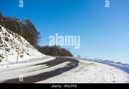 Una strada innevata curva in montagne Vosges (Francia) in inverno con un chiaro e graduate blue sky. Foto Stock