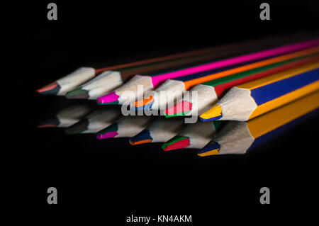 Matite colorate su un vetro riflettente la superficie a specchio. Matite con doppio colore nero su sfondo isolato. Foto Stock