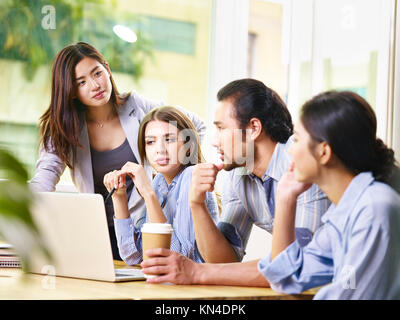 Team di giovani asiatici e caucasici imprenditori maschio e femmina di riunione in ufficio discutere di affari con computer portatile. Foto Stock