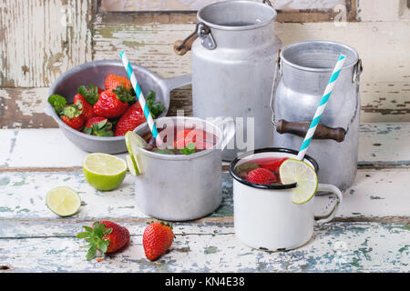 Vintage tazze in metallo con retro cocktail di tubi e acqua-lattine di fragole fatta in casa la limonata, servita con fragole fresche, menta e calce su vecchie wh Foto Stock