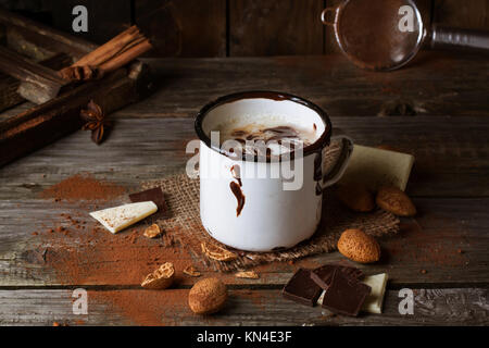 Vintage mug con cioccolata calda servita con pezzetti di bianco e il cioccolato fondente e mandorle sul vecchio tavolo in legno Foto Stock