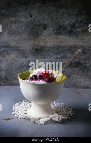 Vaso in ceramica bianca con gelato di vaniglia fatto in casa, servita con un mix di frutti di bosco su metallo grigio nella tabella Foto Stock