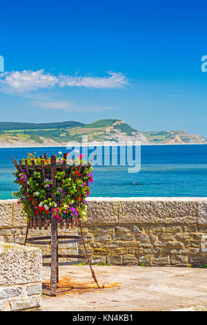 Un basket fuoco con fiori sul lungomare di Lyme Regis con cappuccio dorato al di là su Jurassic Coast Sito Patrimonio Mondiale, Dorset, England, Regno Unito Foto Stock