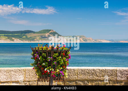 Un basket fuoco con fiori sul lungomare di Lyme Regis con cappuccio dorato al di là su Jurassic Coast Sito Patrimonio Mondiale, Dorset, England, Regno Unito Foto Stock