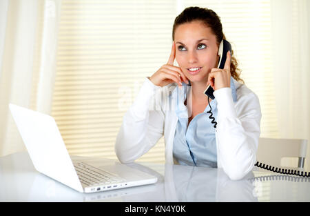 Elegante giovane donna a conversare al telefono nella parte anteriore del computer portatile presso l'ufficio.