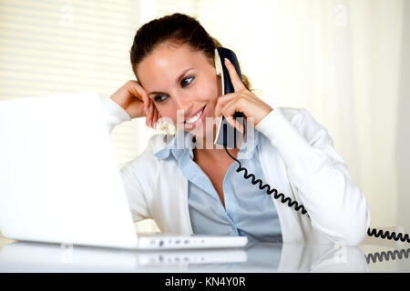Donna sorridente conversare al telefono mentre sta lavorando nella parte anteriore del computer portatile presso l'ufficio.
