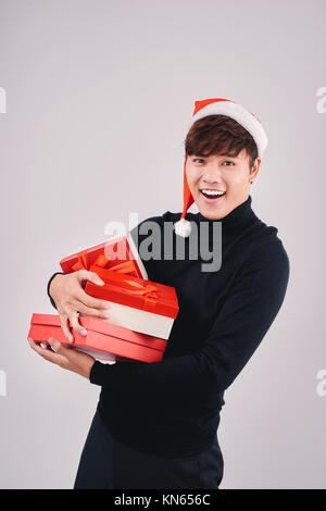 Bel giovane uomo asiatico con santa hat tenendo un dono, isolato Foto Stock